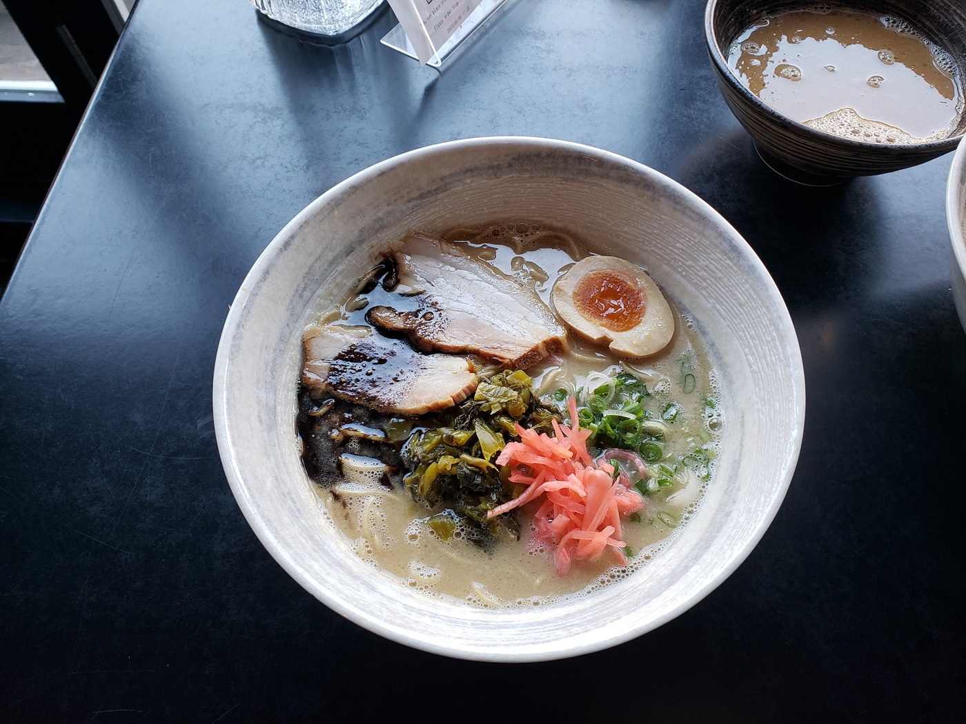 A bowl of tonkotsu ramen with chashu pork, a marinated egg, takana greens and pickled ginger